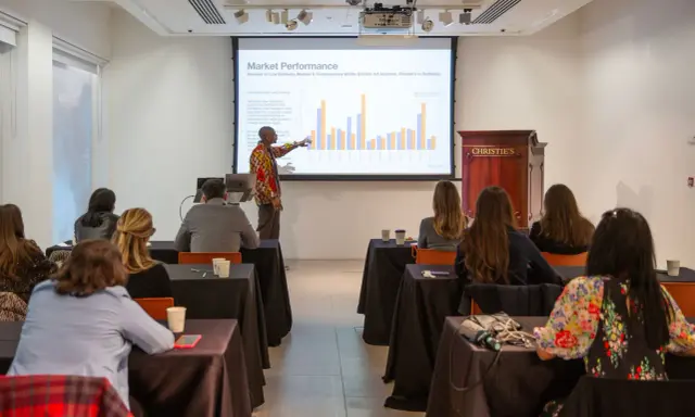 A presenter discusses market performance at Christie's, showing auction data to an audience.