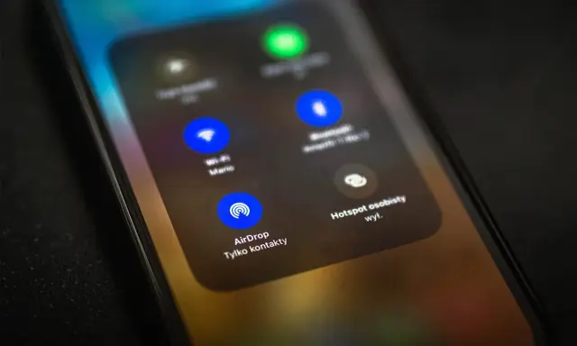 Ekran telefonu z widocznym menu, gdzie opcja AirDrop jest podświetlona. To funkcja do bezprzewodowego udostępniania plików między urządzeniami Apple.