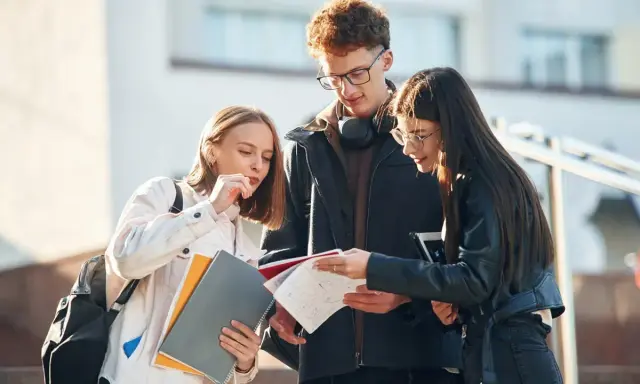 Trzech studentów dyskutuje nad notatkami, ich status ucznia widoczny w skupieniu i materiałach.