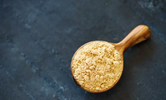 Cuillère en bois remplie de poudre de maca, évoquant ses nombreux bienfaits pour la santé et l'énergie.