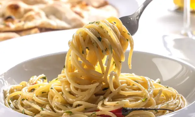Pyszne dania z makaronem: spaghetti z ziołami i czosnkiem, na talerzu, z widocznym w tle pieczywem.
