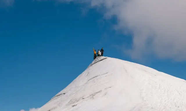 Vandrare på toppen av en snötäckt bergstopp, en vy som ger en känsla av var ligger Kebnekaise.