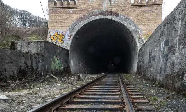 Torowisko prowadzi do ciemnego tunelu pod ceglanym łukiem z blankami, przypominającym bramę do dawnej kopalni Rydułtowy.