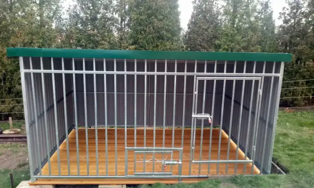 Solidny kojec dla psa z paneli ogrodzeniowych, z drewnianą podłogą i zielonym dachem. Idealne miejsce dla czworonoga.