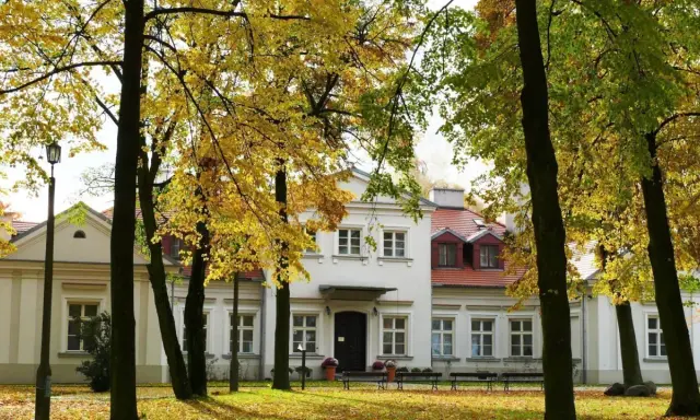 Jesienny spacer wokół dworu Zbożenna. Złote liście drzew otulają zabytkowy budynek.