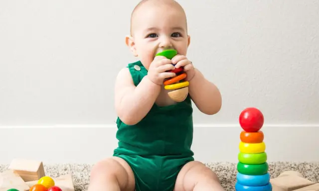 Uśmiechnięte dziecko w zielonym ubranku odkrywa świat, kiedy dziecko chwyta zabawki. Kolorowe klocki i pierścienie zachęcają do zabawy.