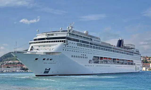 La MSC Armonia, con la sua impressionante lunghezza, solca le acque azzurre vicino a una costa collinare.