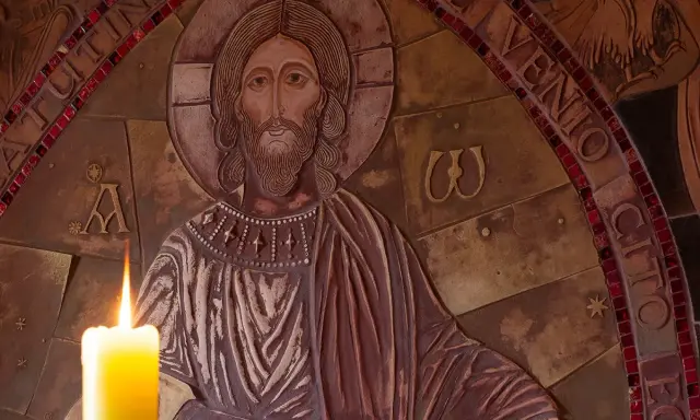 Płonąca świeca przed płaskorzeźbą Chrystusa, symbolizująca modlitwę o spokój i wyciszenie.