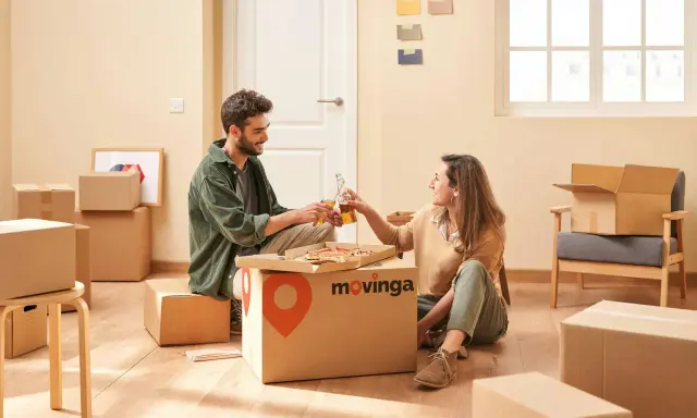 Un couple trinque avec des bouteilles devant une pizza, entouré de cartons. Un avis positif pour Movinga.