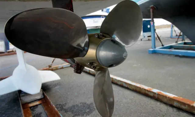 Gros plan sur l'hélice d'un bateau, prête pour son nettoyage. Une autre hélice blanche est visible à gauche.