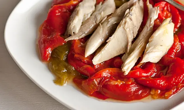 Pimientos asados rojos y verdes con trozos de pescado blanco encima, servidos en un plato blanco.
