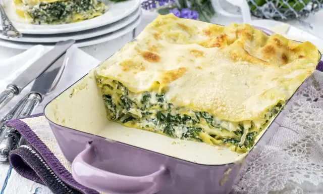 Pyszne lasagne ze szpinakiem w fioletowym naczyniu, gotowe do podania. Obok talerze z porcją i sztućce.
