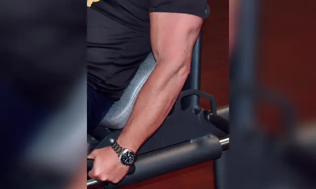Mann trainiert unterarme im gym. Sein Bizeps ist gut sichtbar, während er sich auf ein Gerät stützt.