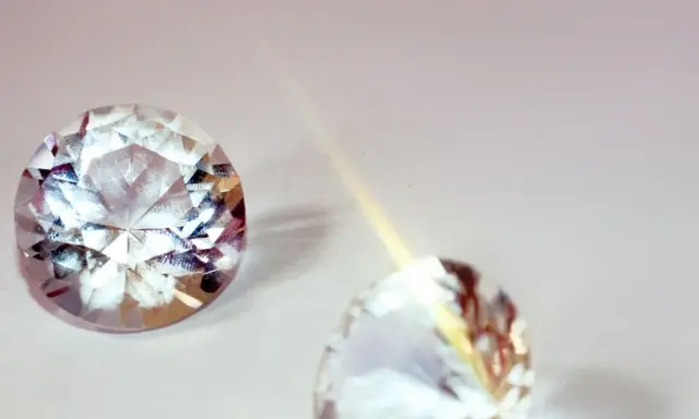Due pietre preziose scintillanti, una sfaccettata e luminosa, l'altra più sfocata, illustrano la differenza tra brillanti e diamanti.
