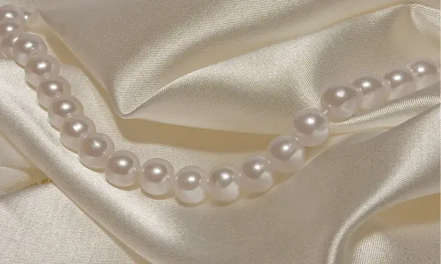 Perły na kremowym jedwabiu. Delikatne fałdy i połysk tkaniny pomogą Ci jak rozpoznać jedwab.
