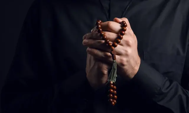 Dłonie księdza trzymające paciorki różańca, symbol wiary i nadziei w obliczu trudów życia, gdzie pańszczyzna a kościół splatały się w historii.