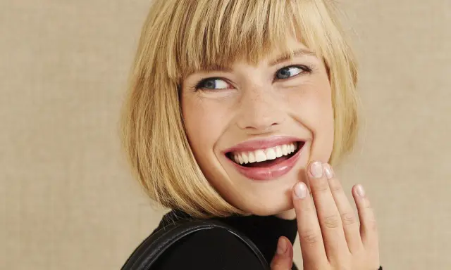 Frau mit blondem Bob, die lacht und ihre Hand vor den Mund hält. Perfekt gestylter Bob.