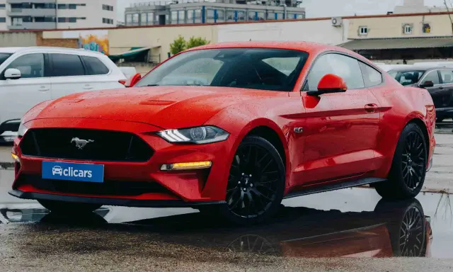 Un deportivo rojo, que es un coche coupe, brilla bajo la lluvia.