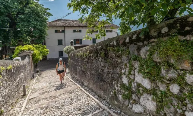 Una donna sale una scalinata di ciottoli verso un edificio bianco, un percorso che ricorda la salita alla Madonna della Corona.