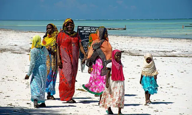 Kobiety w kolorowych strojach spacerują po plaży. Czy Zanzibar to kraj? Tak, to wyspa w Tanzanii.
