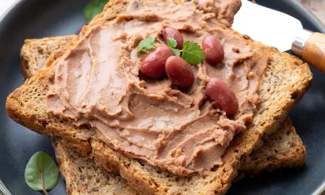 Pyszna pasta z czerwonej fasoli na chrupiących tostach, ozdobiona fasolkami i listkami ziół. Idealna na szybkie śniadanie.
