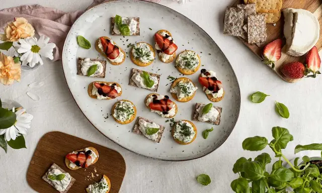 Vackra midsommar-snittar med ost, jordgubbar och örter på en stor tallrik. Perfekt för sommarfesten!