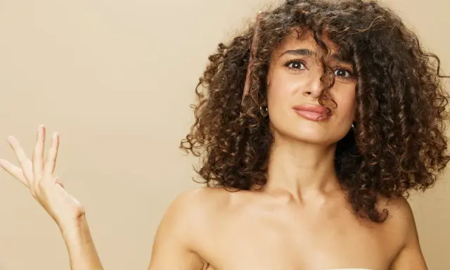 Une femme aux cheveux bouclés tente de diminuer le volume de sa chevelure avec un peigne.