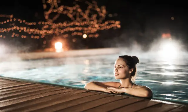 Entspannter Abend in den Thermen NRW. Eine Frau genießt das warme Wasser, umgeben von stimmungsvoller Beleuchtung und Dampf.
