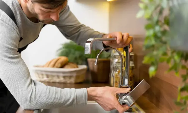 Hombre ajustando grifo de cocina para regular la presión del agua en casa.