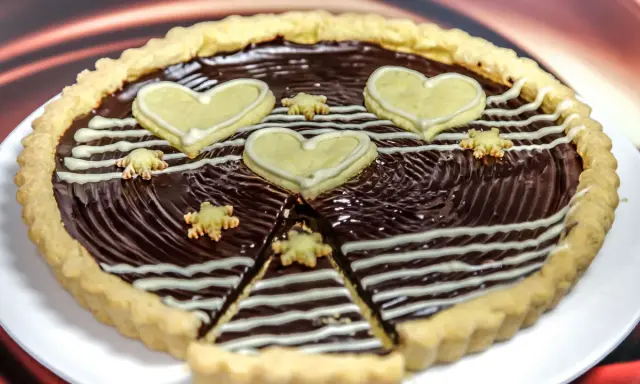 Una deliziosa crostata al cioccolato, decorata con cuori e fiorellini di pasta frolla, pronta per essere gustata.