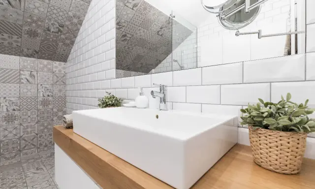 Salle de bain moderne avec lavabo rectangulaire, robinetterie chromée et un mur orné de **pose carrelage mural** patchwork gris et blanc.