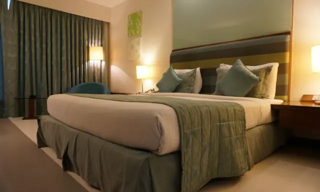 Ideas de iluminación para dormitorio de matrimonio: cama acogedora con lámparas de noche y cortinas verdes.