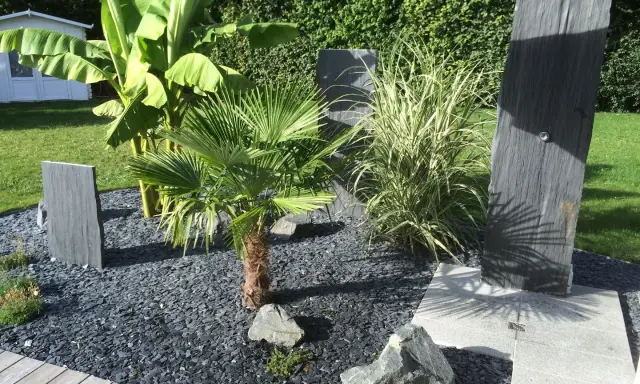 Une belle entrée de maison extérieure avec une plante luxuriante, des ardoises et un palmier.