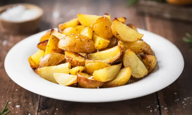 Patate al forno con buccia, dorate e croccanti, servite su un piatto bianco. Un contorno semplice e gustoso.