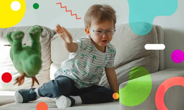 Un bambino super attivo gioca sul divano con un pupazzo verde. Le sue mani sono in movimento, pronto a interagire con il giocattolo.