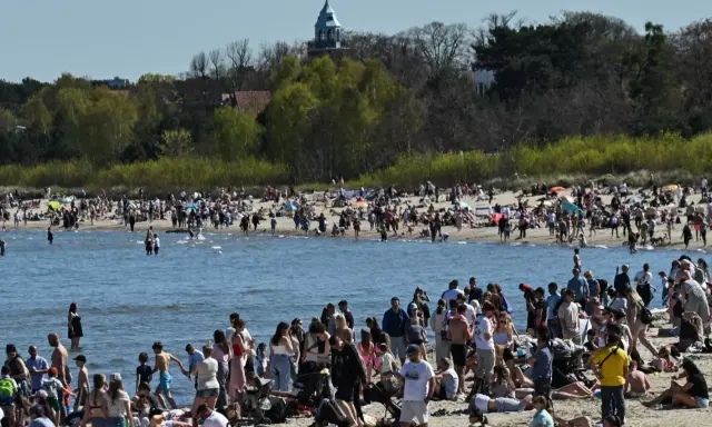 Tłumy ludzi na plaży, woda i zielone drzewa w tle. Widać wieżę kościelną. Ceny nad morzem pewnie wysokie, ale widok piękny.