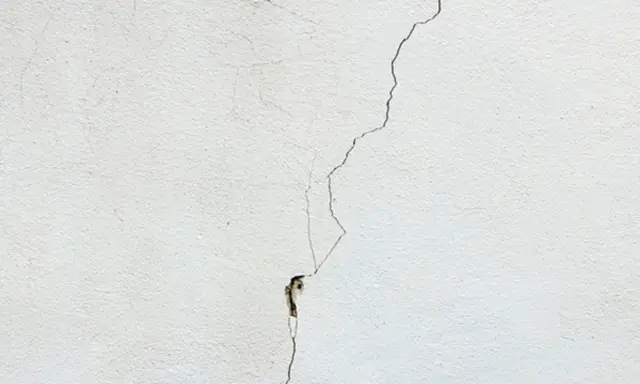 Una grieta fina y profunda recorre una pared blanca, mostrando diferentes tipos de grietas en techos y paredes.
