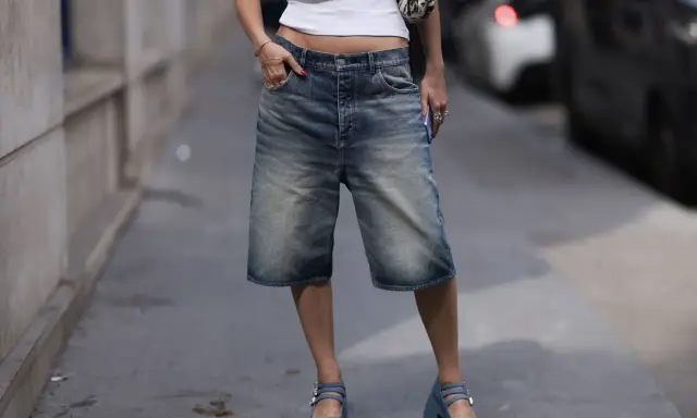 A person in denim bermuda shorts and a white crop top sports chunky blue platform Mary Janes, a nod to early 2000s shoe trends.