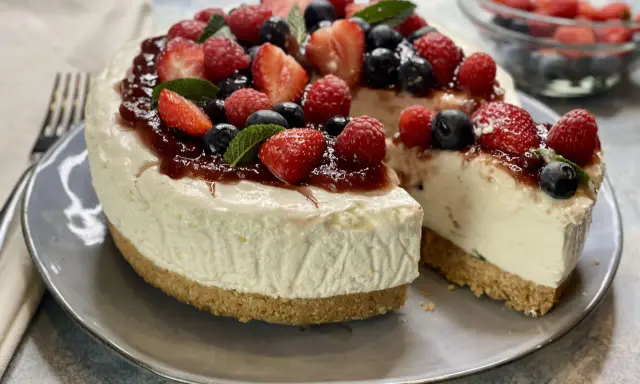 Deliziosa torta fredda allo yogurt, guarnita con fragole, lamponi, mirtilli e una colata di marmellata. Perfetta per un dessert estivo.