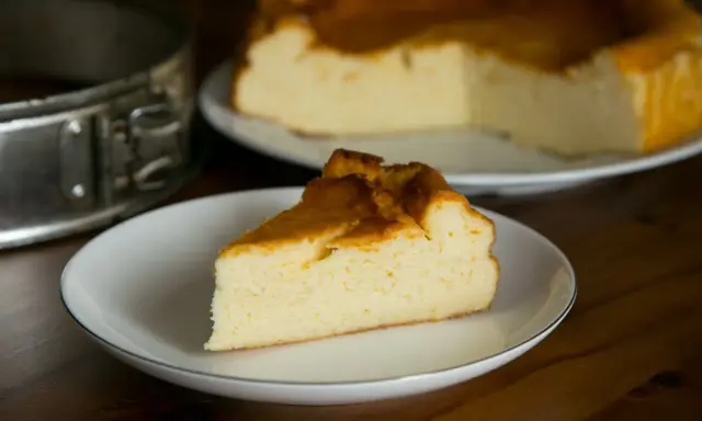 Puszysty sernik z mlekiem skondensowanym, z rumianą skórką, na talerzyku. Obok forma do pieczenia.