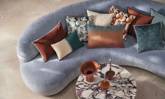 Tante idee cuscini divano: tonalità calde e fredde, fantasie geometriche e texture vellutate su un divano grigio.