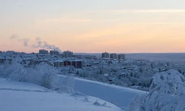 Vinterlandskap i lapponia svedese med snötäckta träd och byggnader i fjärran under en rosa solnedgång.