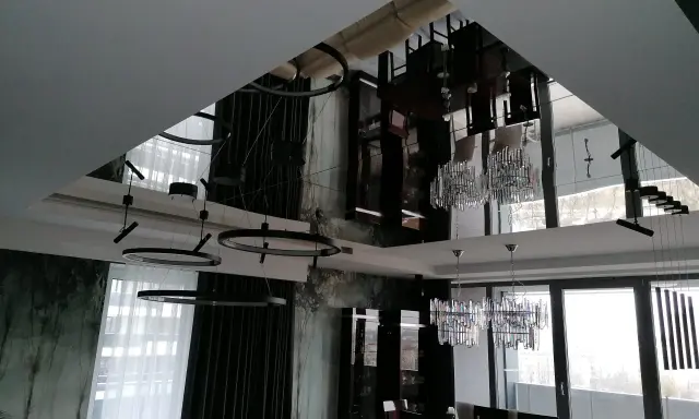 Eleganckie lustro na suficie w sypialni odbija nowoczesne lampy i meble, tworząc wrażenie przestronności.