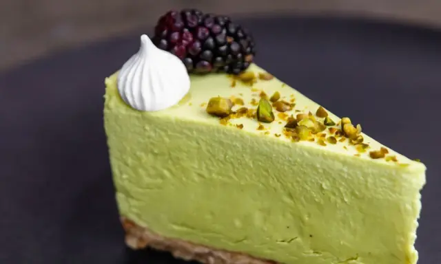 Pyszny sernik pistacjowy na zimno, udekorowany pianką, jeżyną i posypany pistacjami.