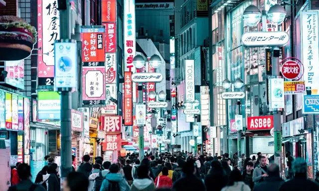Eine belebte Straße mit vielen leuchtenden Neonschildern, die Geschäfte und Restaurants bewerben. Dies ist ein typisches Beispiel für einen urbanen Raum, voller Leben und Aktivität.
