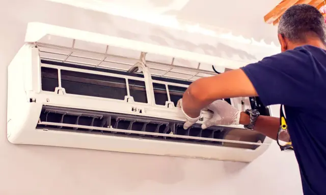 Un technicien en gants blancs effectue le nettoyage de climatisation, ouvrant l'unité pour accéder aux composants internes.