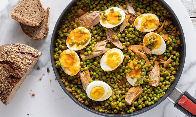 A skillet of peas and tuna with sliced hard-boiled eggs, served with bread.