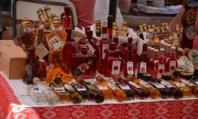 Różnorodne butelki z rakiją, w tym te w kształcie kobiecym, oferowane na targu. Co to rakija? To tradycyjny alkohol, często owocowy.