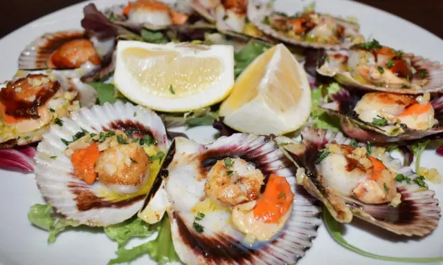 Zamburiñas congeladas a la plancha, doradas y jugosas, servidas en sus conchas con limón y hierbas.
