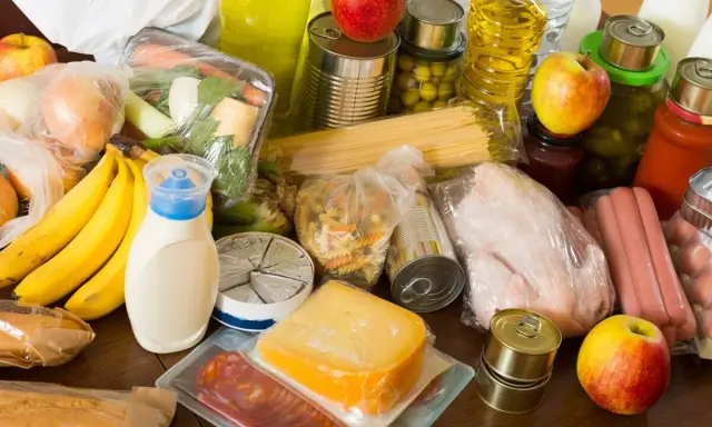 Variedad de alimentos, incluyendo frutas, verduras, pasta, latas y embutidos, que representan alimentos procesados y frescos.
